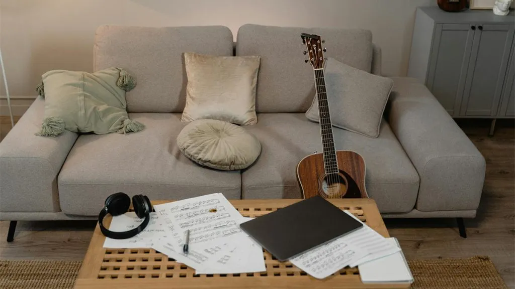 Guitar and sheet music laid out on a coffee table and couch